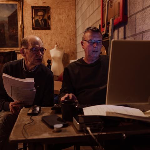 Twee vrijwilligers zitten aan de computer en voeren gegevens van een papieren fiche in in de databank.