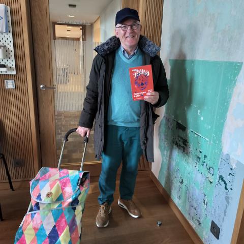 Vrijwilliger poseert met boodschappentrolley en een folder van Erfgoeddag in de hand.