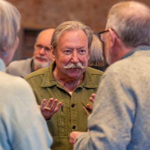 Vrijwilliger met grote snor en groen hemd praat met twee andere vrijwilligers